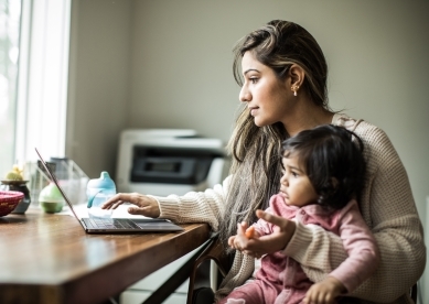 Mother working on a laptop at a table with her daughter on her lap